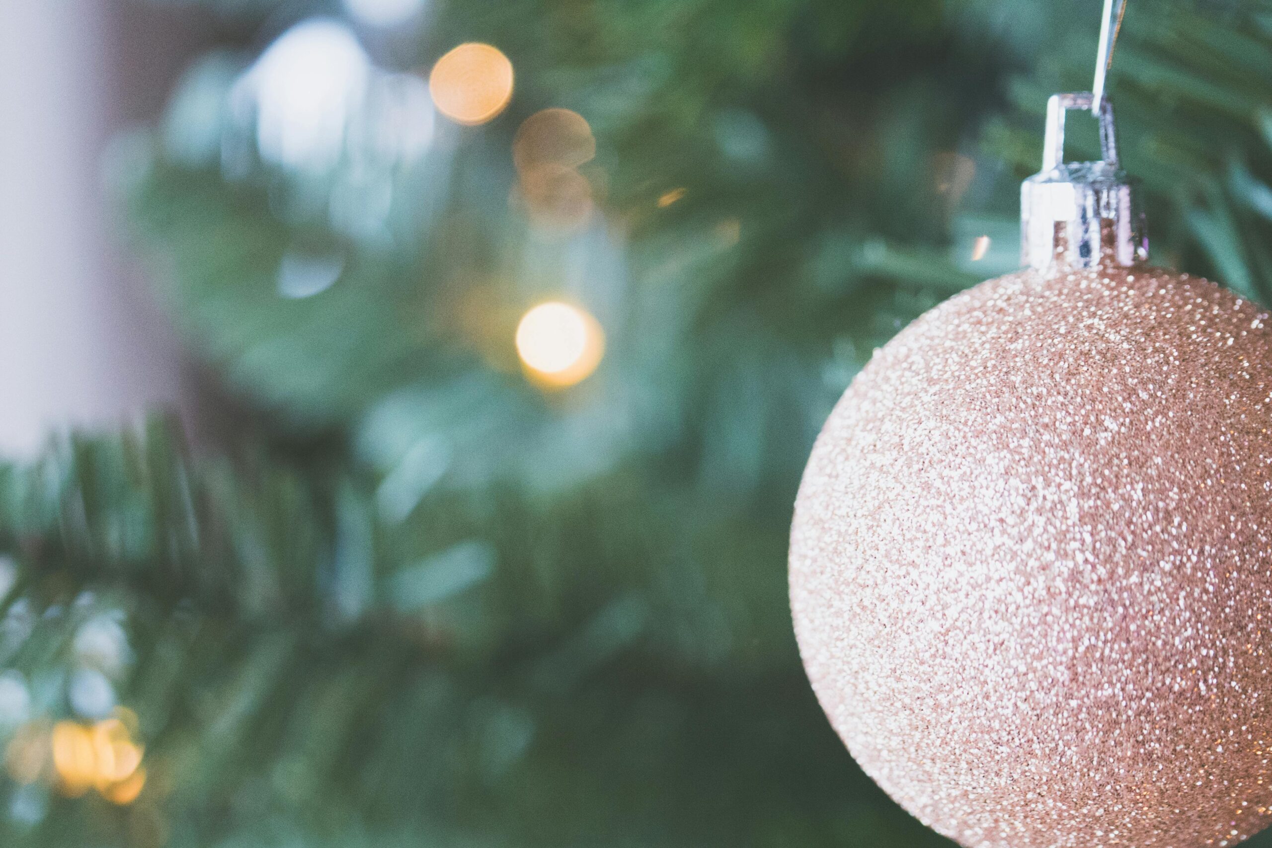 Close-up of a glittery gold Christmas ornament hanging on a tree branch indoors.