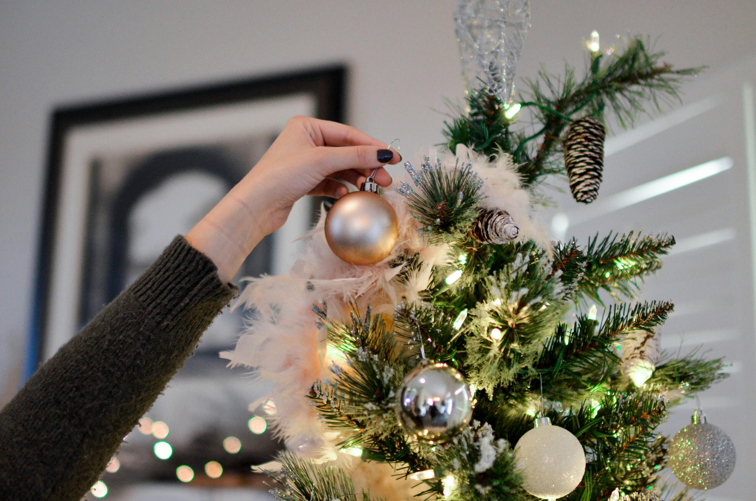 A hand decorates a Christmas tree with shiny ornaments, capturing the festive spirit.